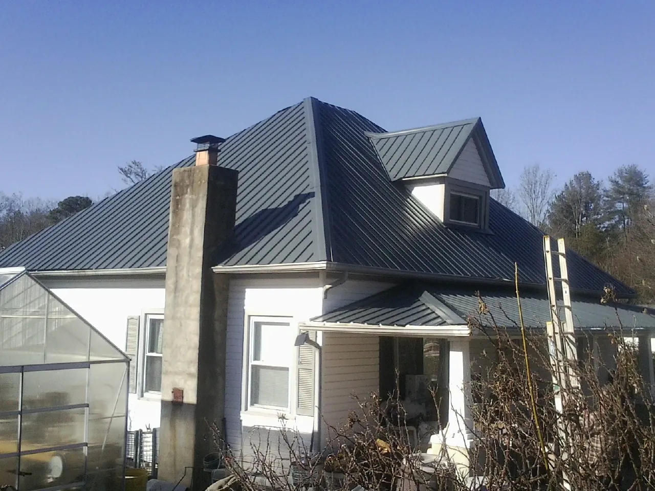 Dark blue standing seam metal roof on a white farmhouse with dormer — Slate & Tile Roof Repair by Roofing Brothers in Flowery Branch