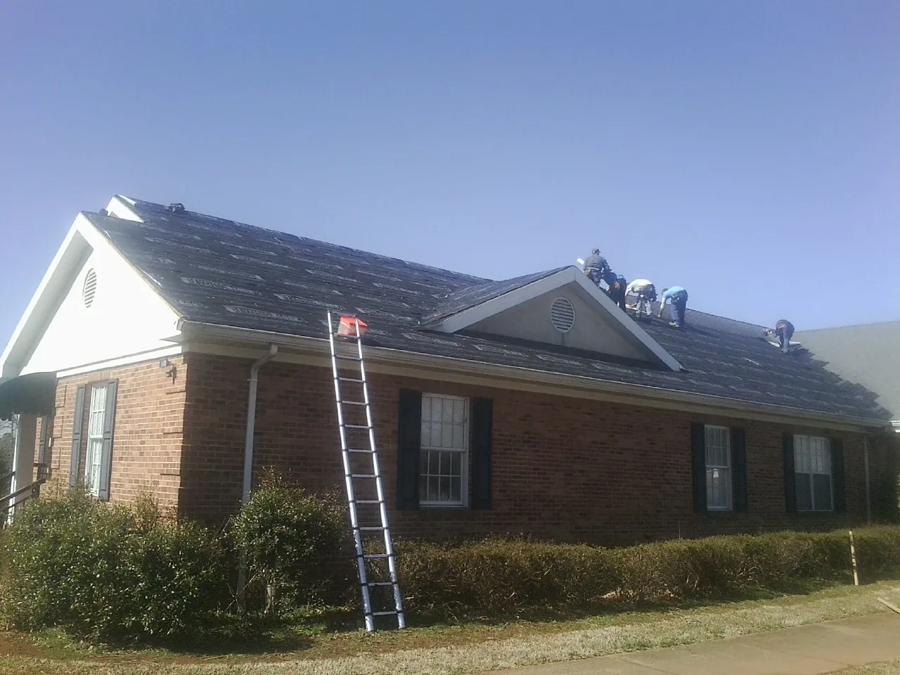 Crew tearing shingles off a brick ranch roof with a ladder set — Metal Roof Repair work by our crew in Flowery Branch