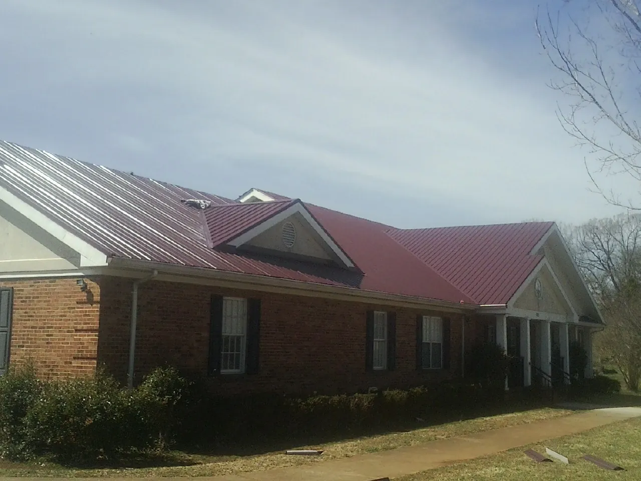 Red metal roof with gabled entries on a long brick building, from a Hail Damage Roof Repair job in Flowery Branch