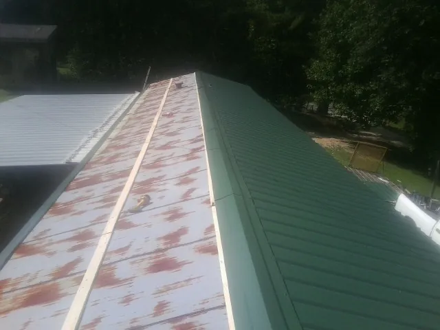 Old rusted panels beside newly installed green metal roofing — Wind Damage Roof Repair by Roofing Brothers in Flowery Branch