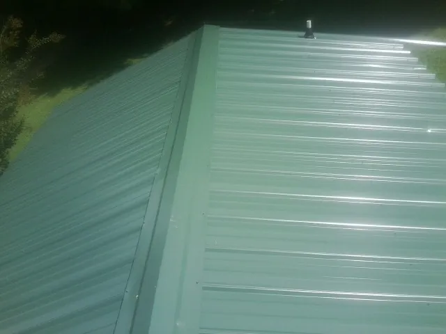 New green metal panels meeting at the ridge of a roof — Flat Roof Repair work by our crew in Flowery Branch