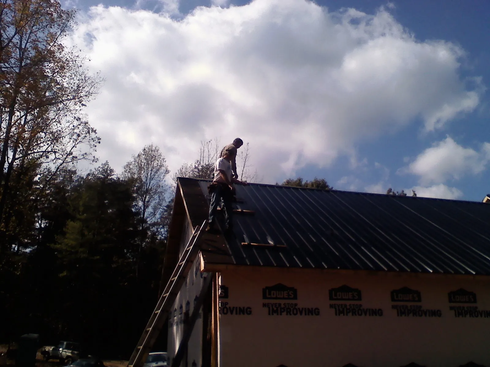 Roofer fastening dark metal panels high against a cloudy sky, from a Roof Inspection job in Flowery Branch