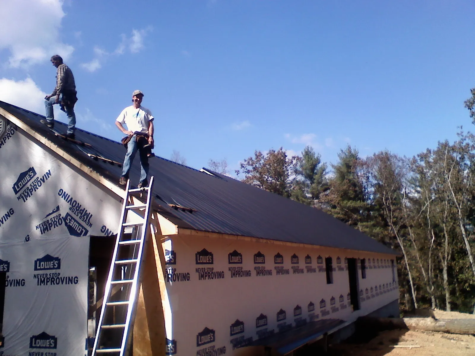Two roofers standing on a long dark metal roof over a wrapped building in Flowery Branch