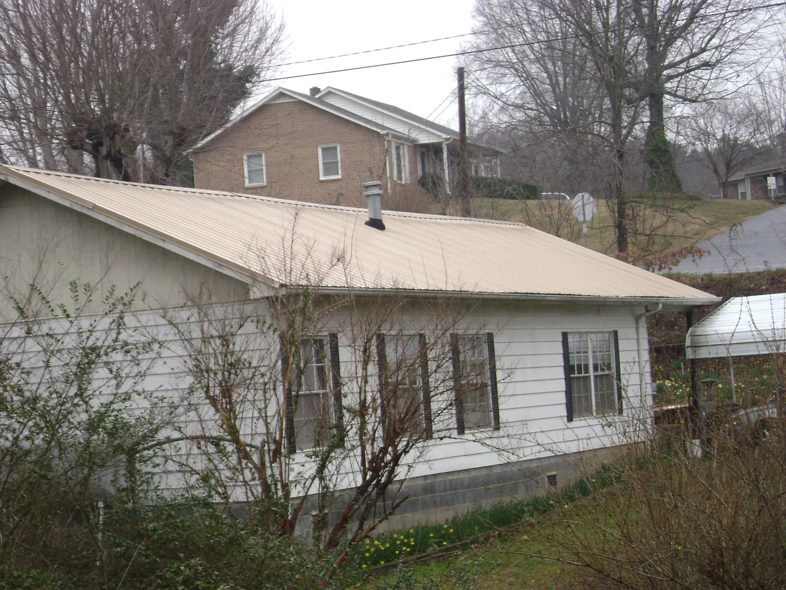 Tan metal roof on a white sided house set into a hillside — Commercial Roofing by Roofing Brothers in Flowery Branch
