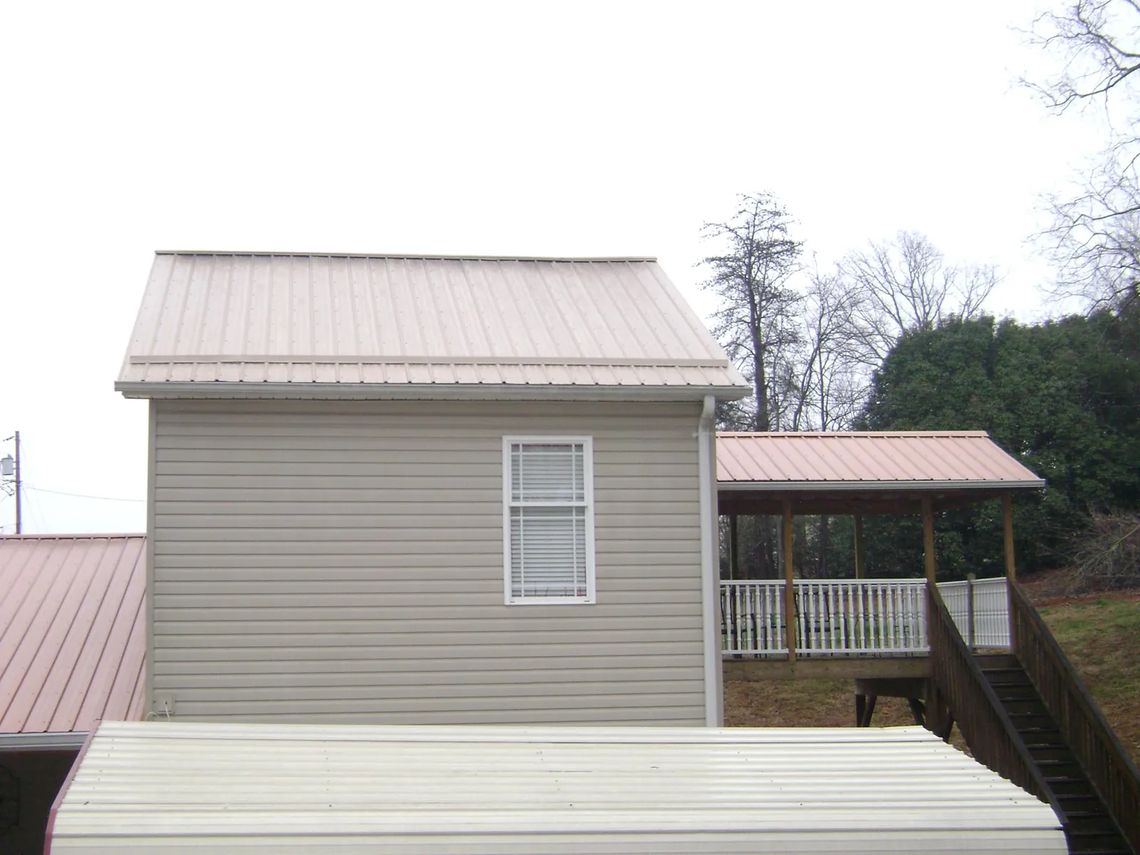 Tan metal roofs on a two story addition and attached porch, from a Roof Replacement job in Flowery Branch